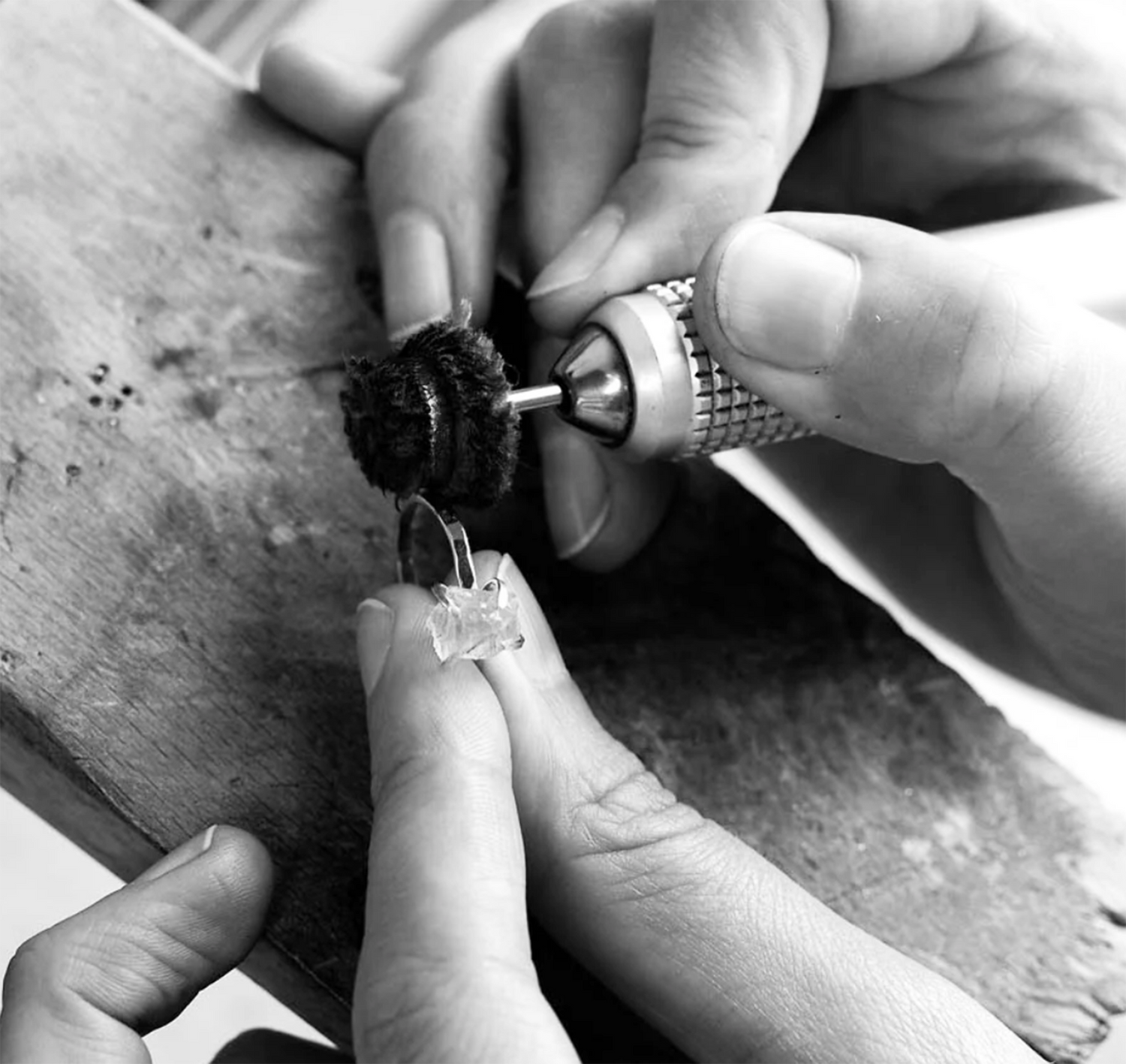 Close-up of a jeweller polishing a ring with a handheld rotary tool, holding the ring steady on a workbench.