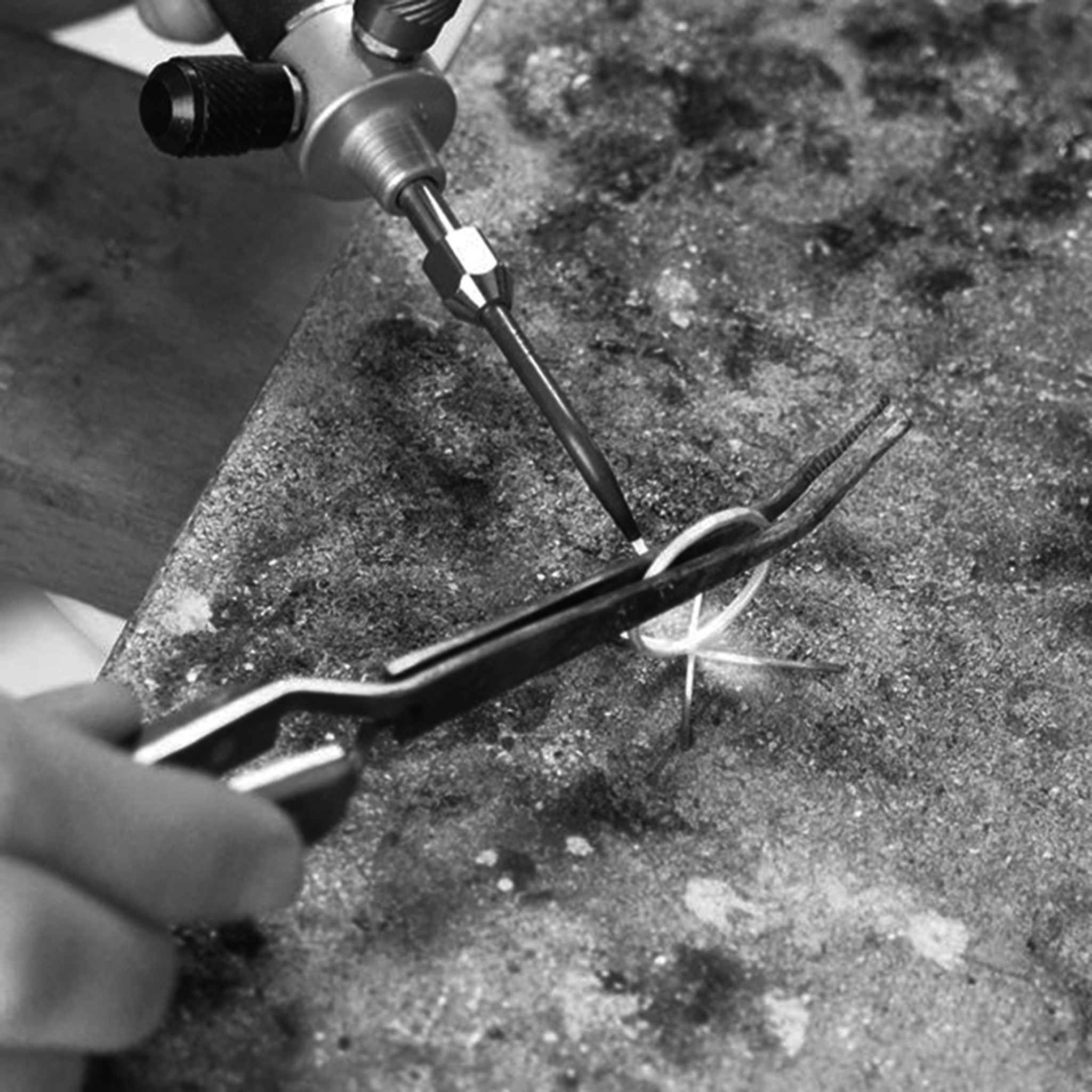 Close-up of a jeweller using a blowtorch to solder a ring held in place with pliers.