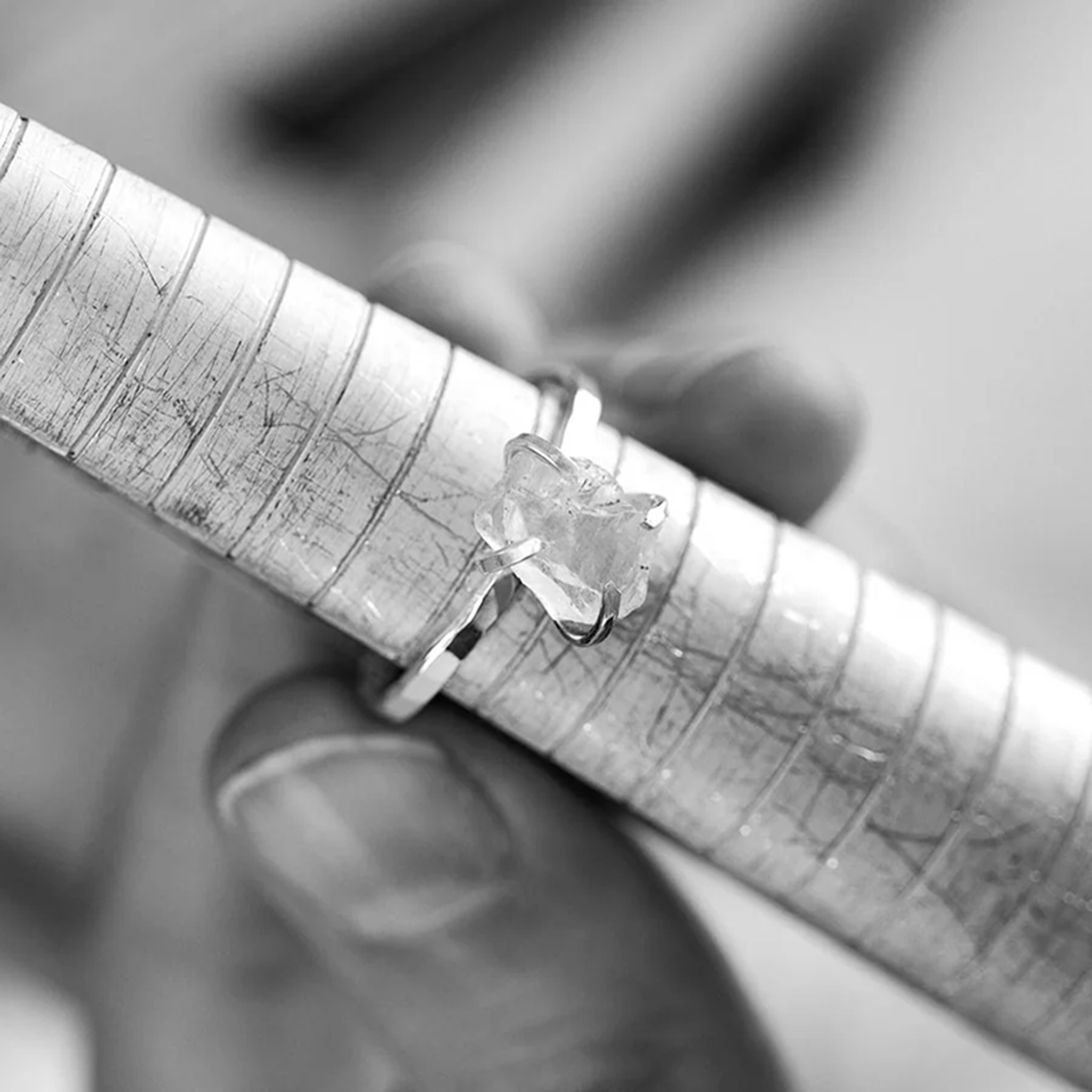 A jeweller holding a ring with a raw gemstone against a ring mandrel for sizing.