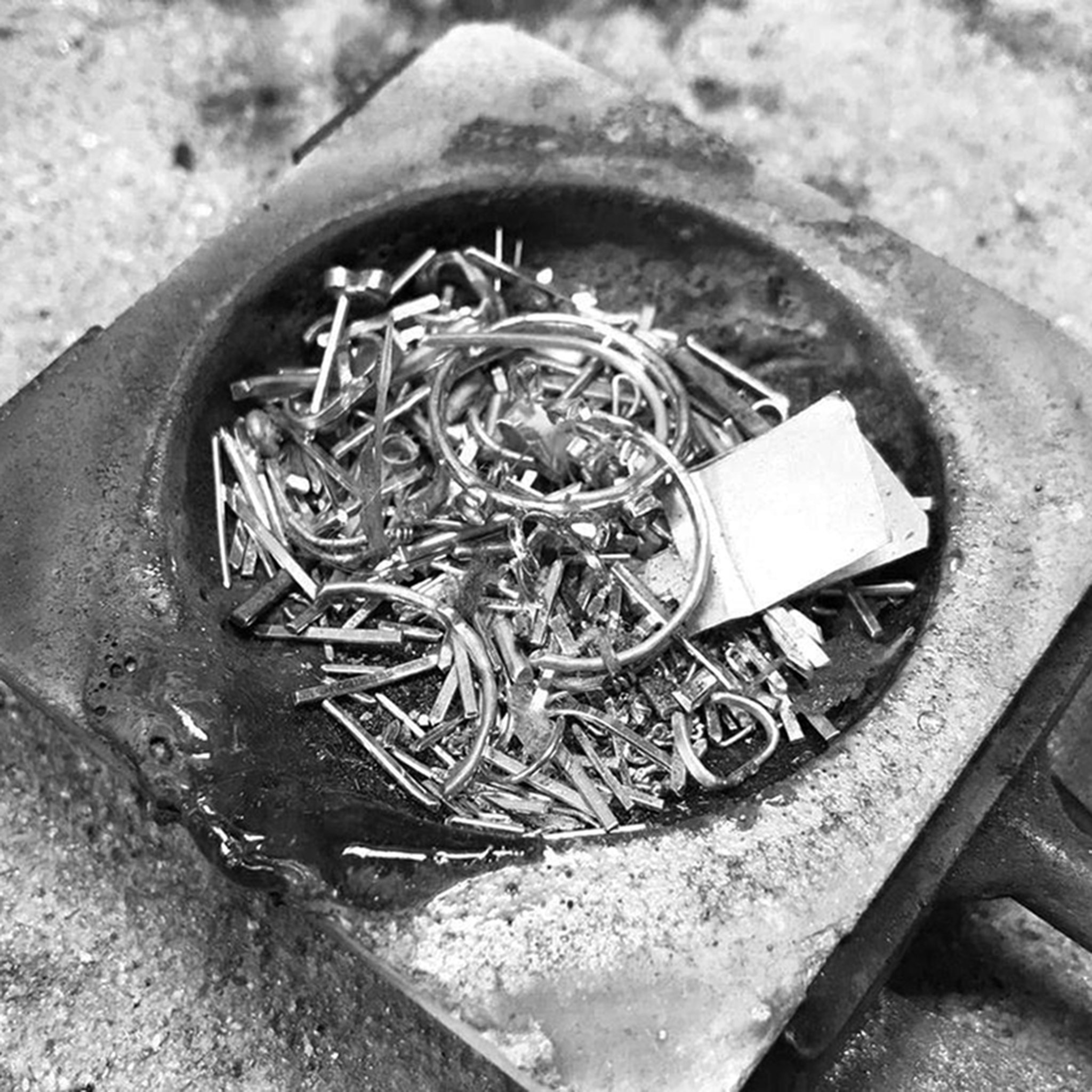 A small pile of silver or gold scrap metal, including wires and offcuts, on a jeweller’s soldering block.